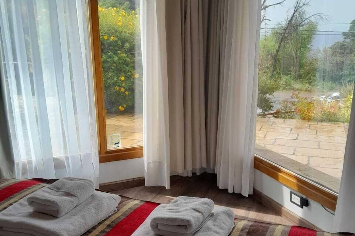 Habitación de hotel con un ventanal grande, dos toallas sobre un felpudo a rayas y vistas al exterior con vegetación.