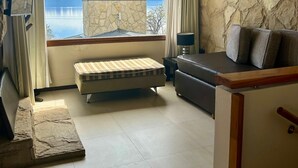 Une chambre avec un lit, un canapé, une télévision et une vue sur un lac et des montagnes.