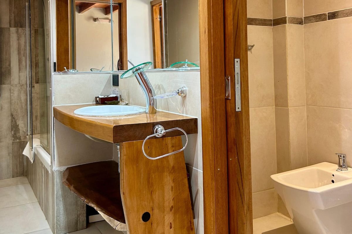 Un baño moderno con tocador de madera, cabina de ducha de vidrio, espejo grande y zona separada para lavamanos e inodoro.