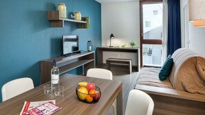 Una habitación de hotel moderna con una mesa de comedor de madera, un sofá, un televisor y un ventanal con cortinas.