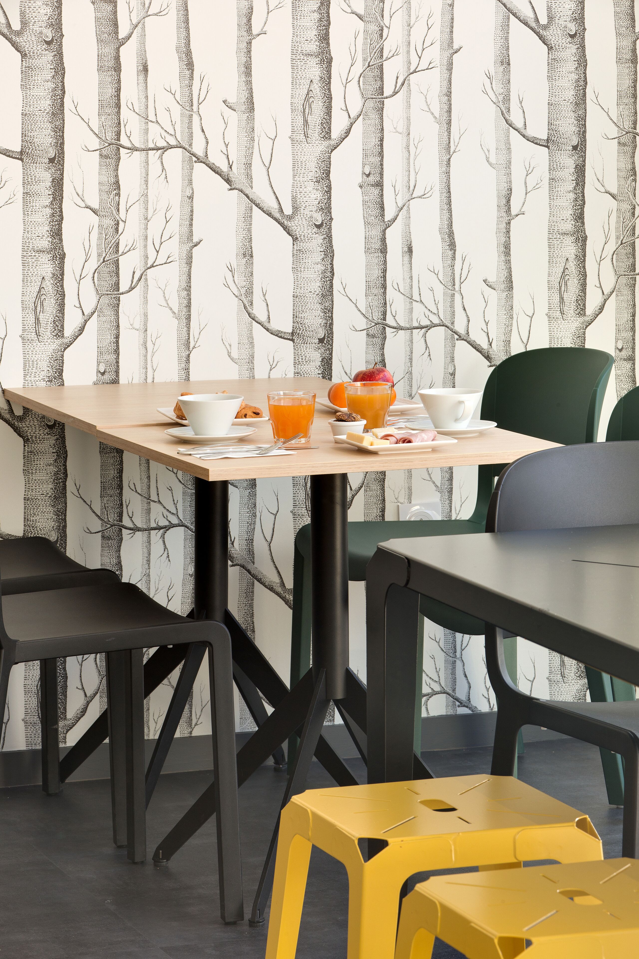 A dining area with a table set for breakfast, including a cup, a bowl, a plate with food, and a glass of orange juice.