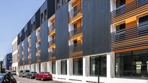 Un edificio moderno de varios pisos con balcones, ventanas amplias y un estacionamiento con automóviles.