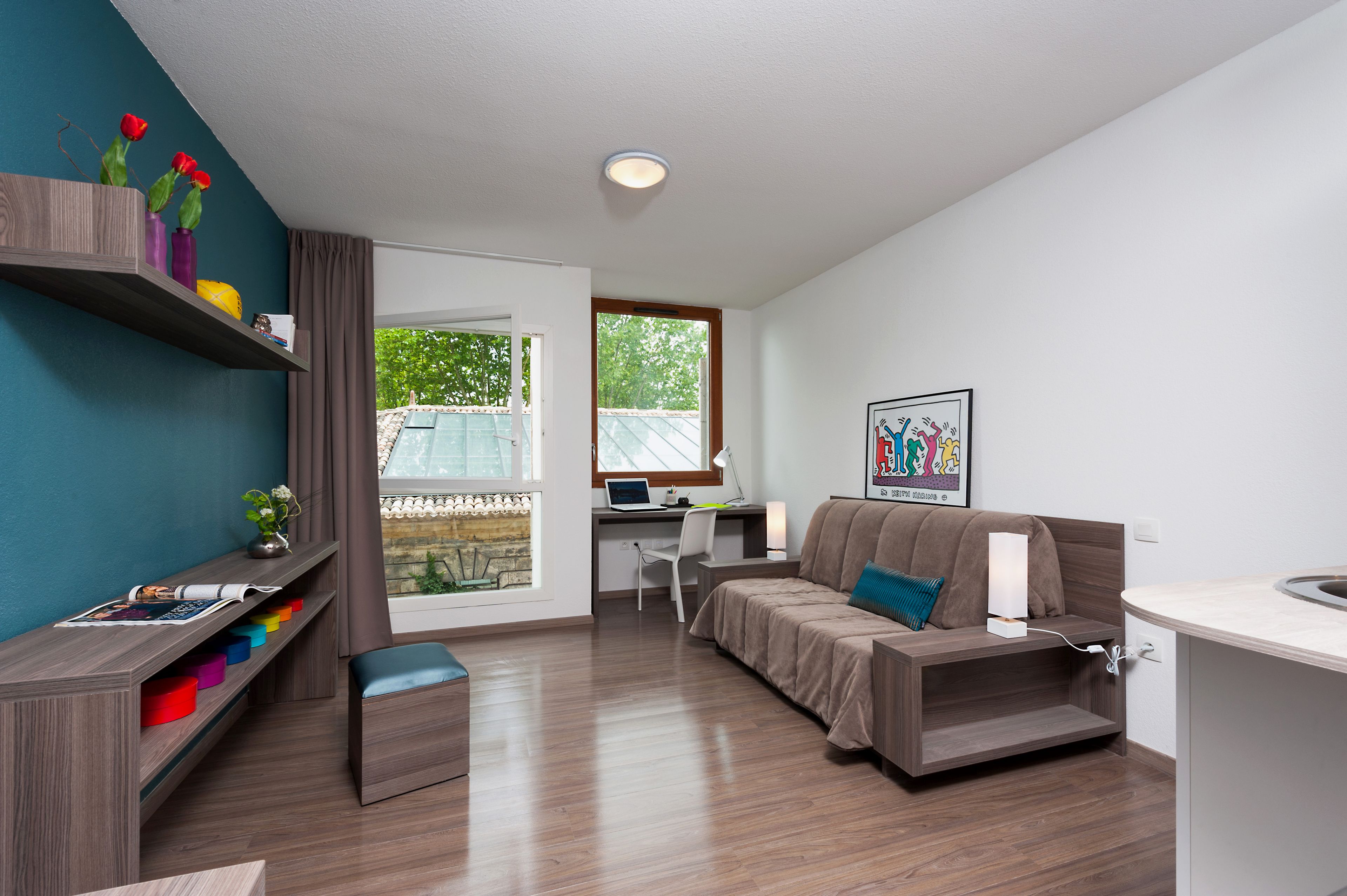 A modern room with a sofa, a desk, and a small kitchen area.