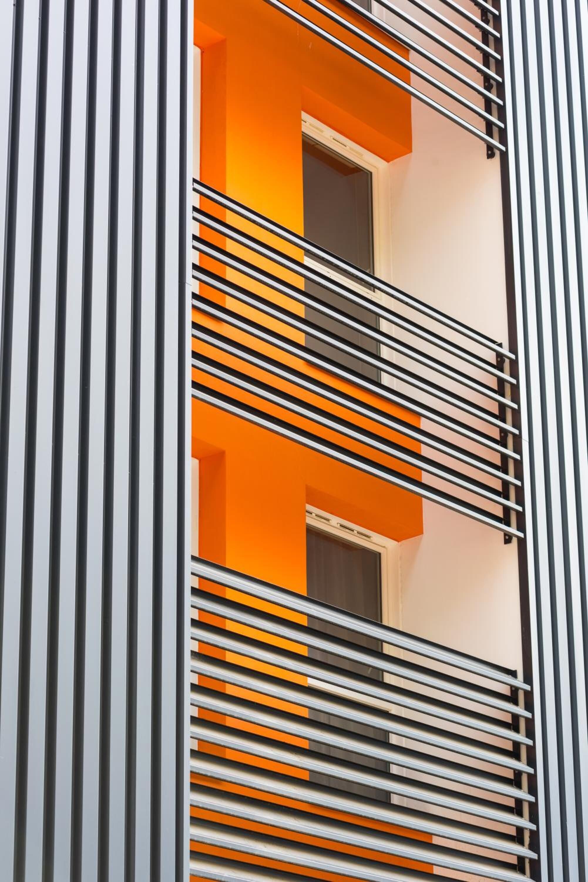 A modern building facade with vertical black and white striped patterns and a section with orange and white walls.