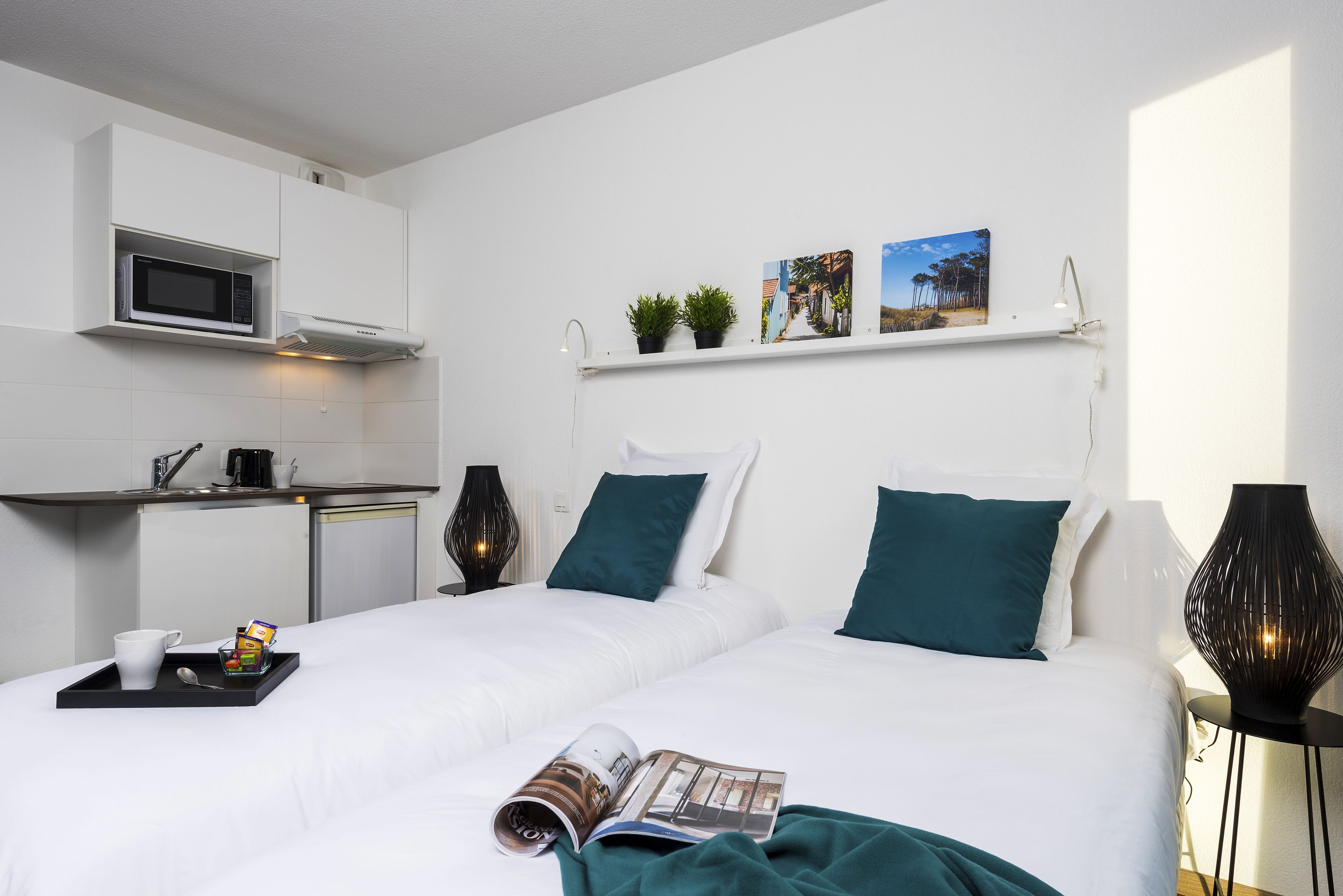 A modern hotel room with two beds, a kitchenette, and a small dining area.