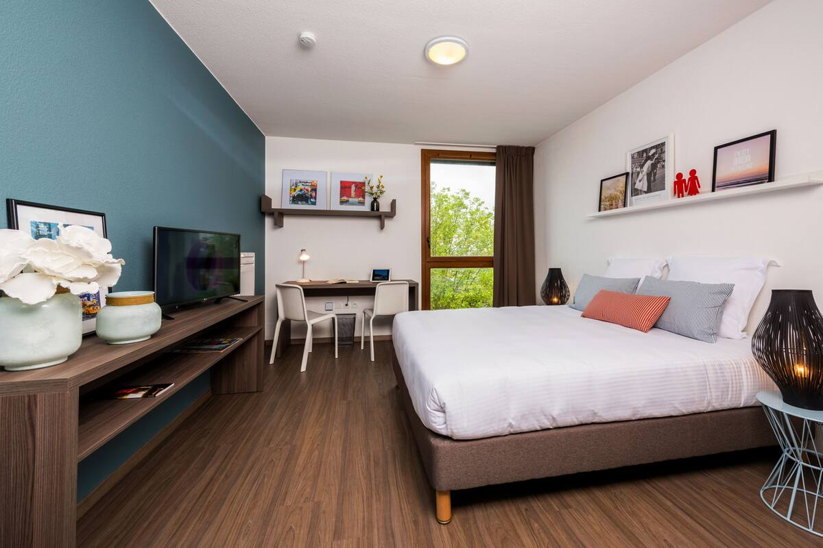 A modern bedroom with a bed, desk, and TV.