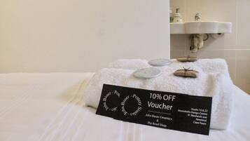 A neatly made bed with a towel and a voucher for a 10% discount at The Bead Shop.