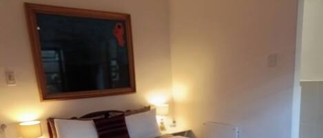 A neatly made bed with white linens and a red blanket, two bedside lamps, and a framed picture on the wall.