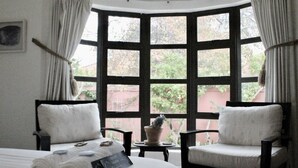 A room with a large bay window, two chairs, a bed with rolled towels, and a small table with a potted plant. - The John Bauer Pottery Studio (Cape Town)