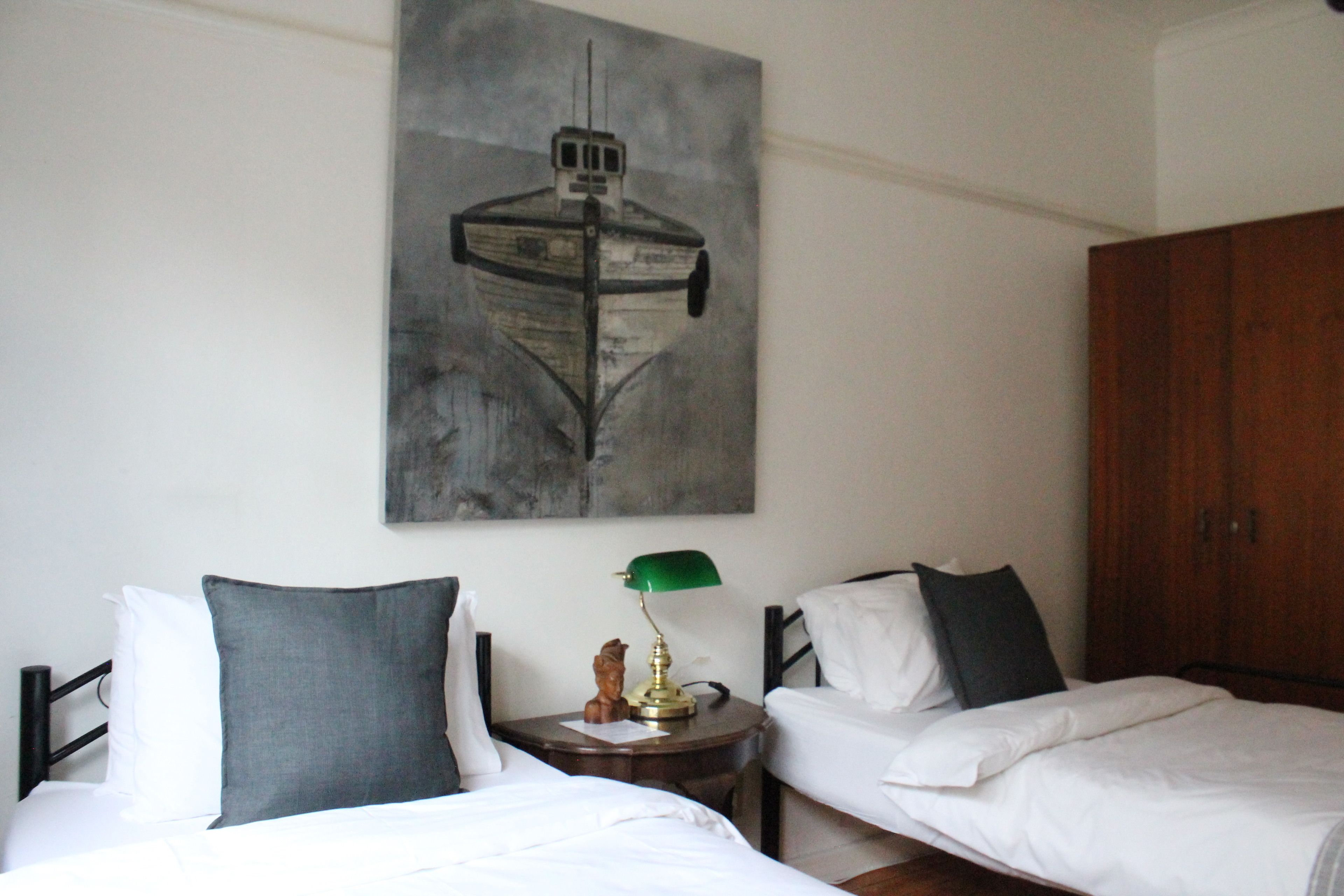 Camera d'albergo con due letti, un armadio in legno, un quadro appeso e un comodino con una lampada.