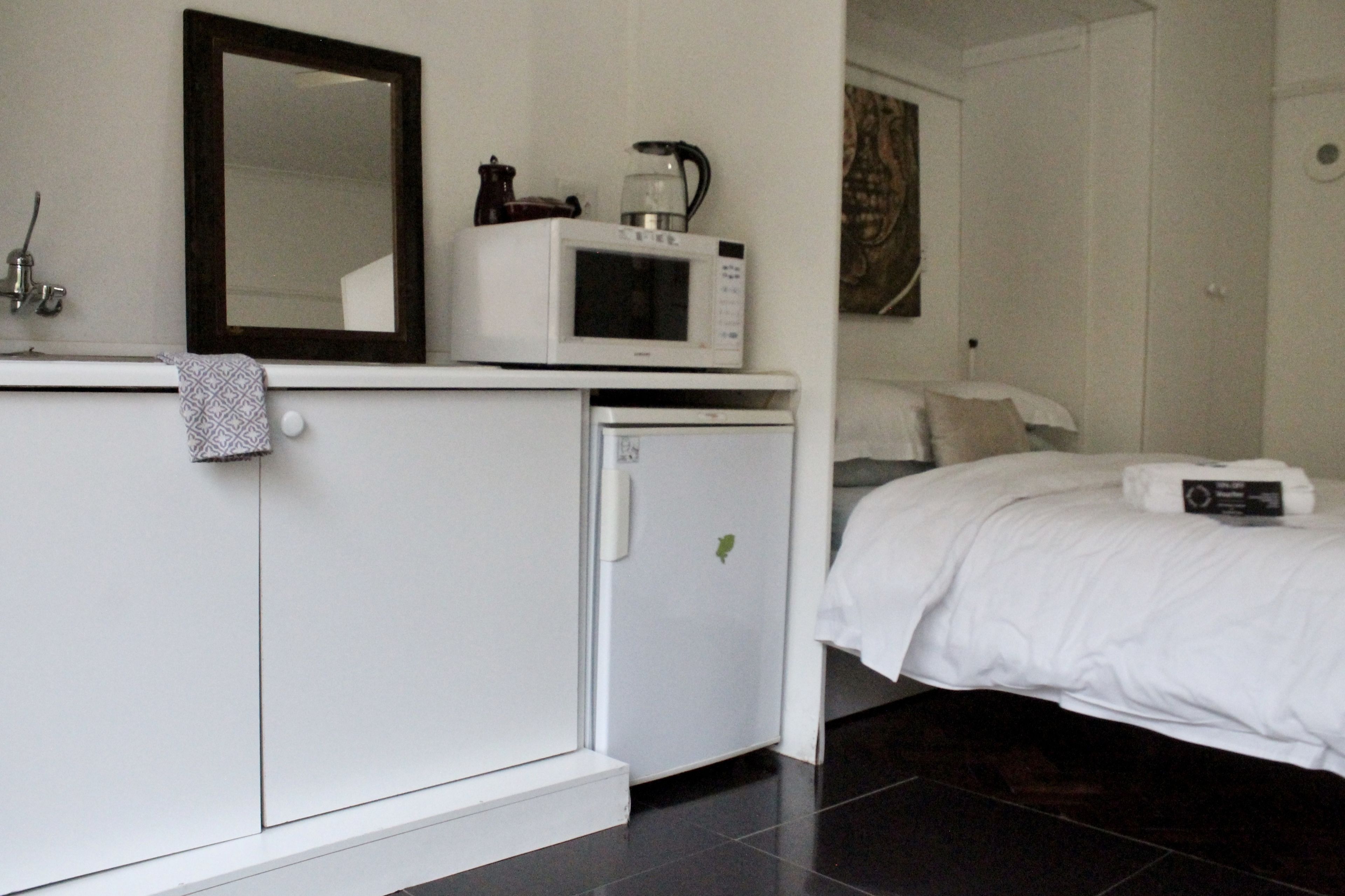 Une chambre d’hôtel avec un lit, un petit réfrigérateur blanc, un four à micro-ondes, une machine à café et un miroir au mur.