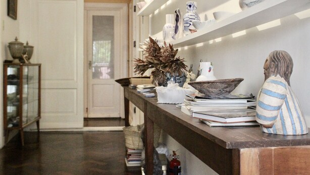 A hallway with a wooden reception desk, shelves with decorative items, and a door in the background. - The John Bauer Pottery Studio (Cape Town)