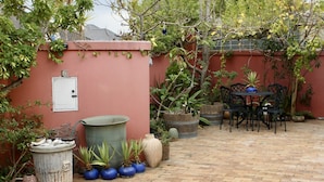 A patio area with a brick floor, a red wall, and various potted plants. - The John Bauer Pottery Studio (Cape Town)