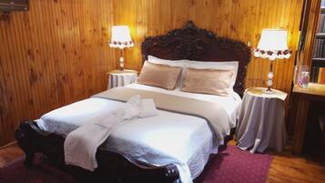 A wooden-paneled room with a large bed, two bedside tables with lamps, and a bookshelf.