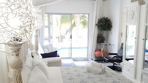 A spacious bedroom with a large bed, a sitting area with a chair and a table, a potted plant, and a view of the outdoors.