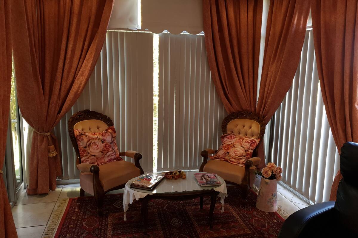 A room with two upholstered chairs with floral upholstery, a small table with a magazine, and a vase with flowers.