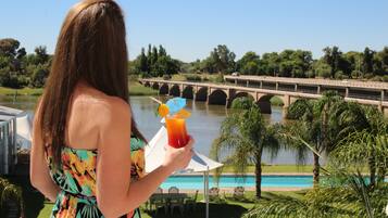 Una mujer sostiene una bebida con sombrilla tropical, con vistas a un puente y una piscina.