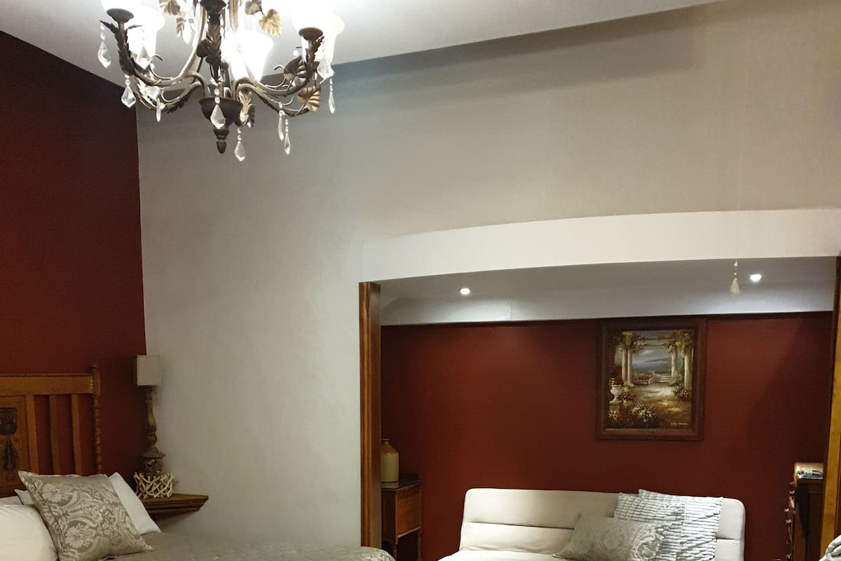 A bedroom with a bed, a sofa, a chandelier, and a painting on the wall.