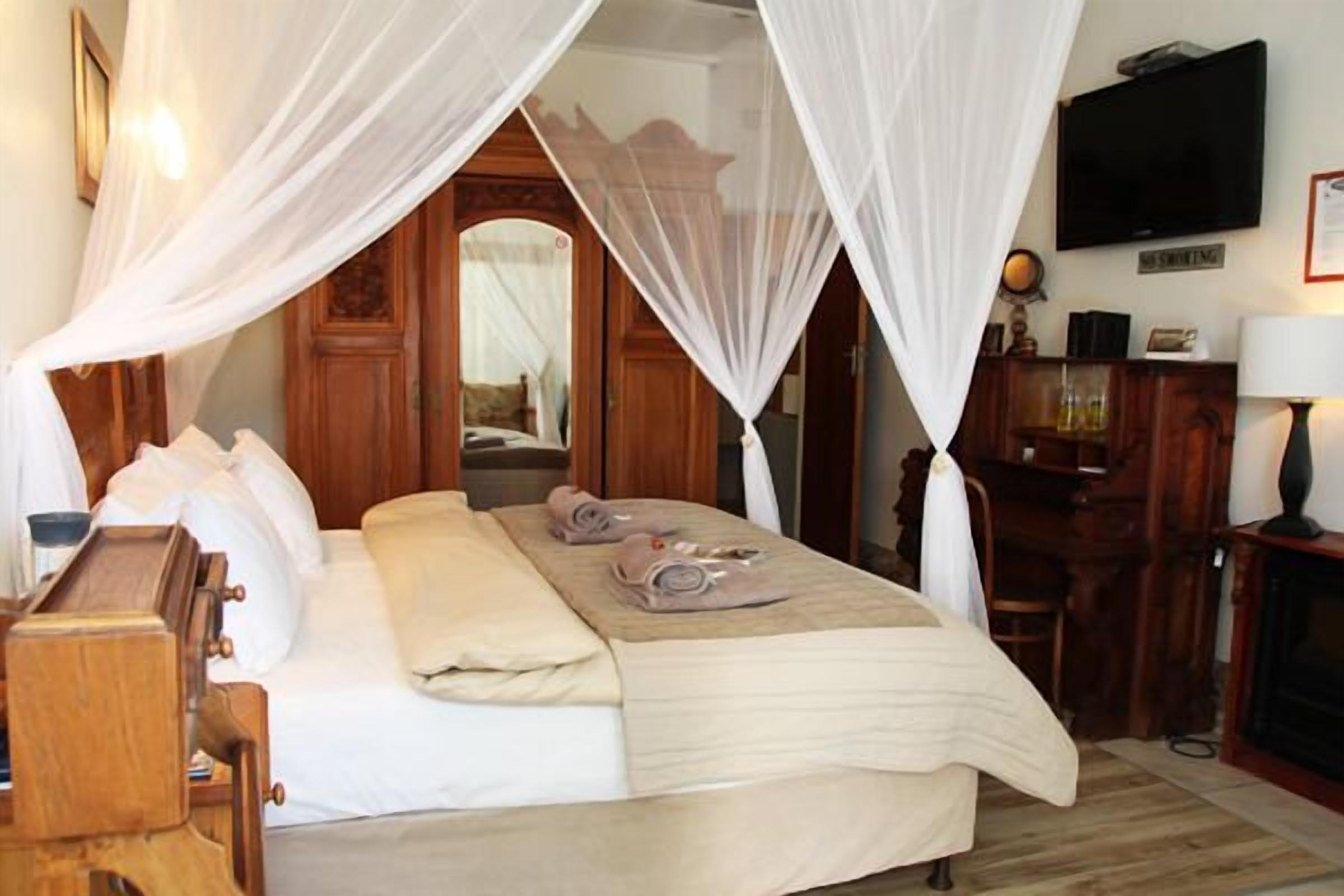 A hotel room with a bed, wooden furniture, a television, and a desk with a lamp.
