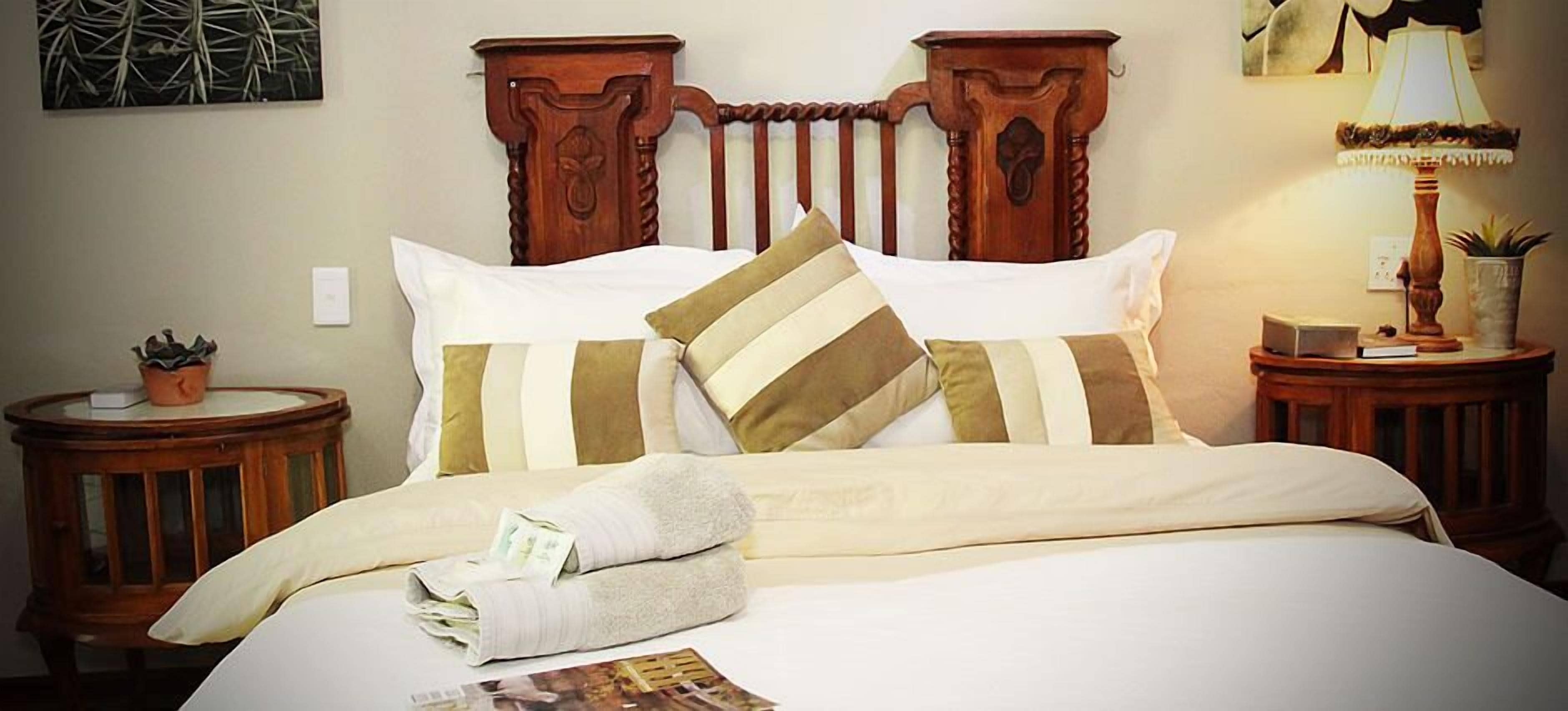 A neatly made bed with striped pillows, a wooden headboard, and a bedside table with a lamp and a plant.