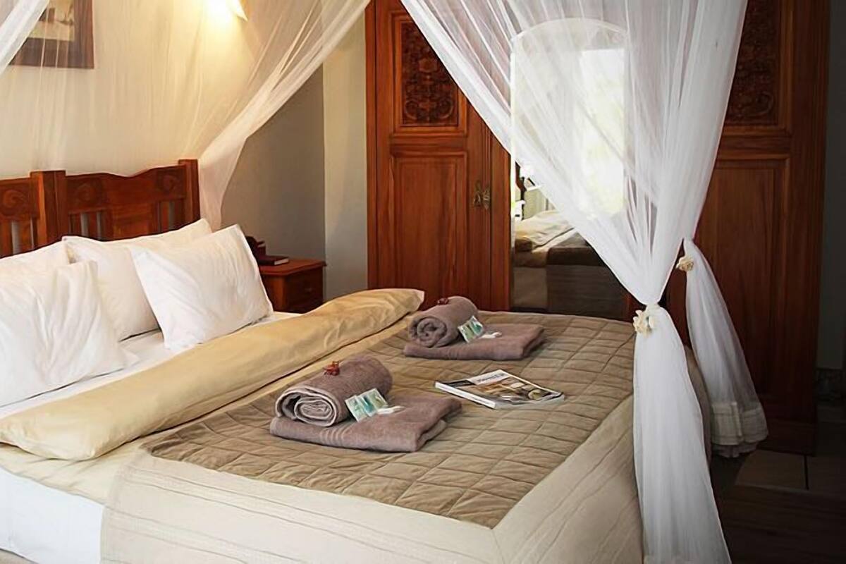 A neatly made bed with white and beige bedding, a wooden headboard, and a nightstand with a water bottle and a book.
