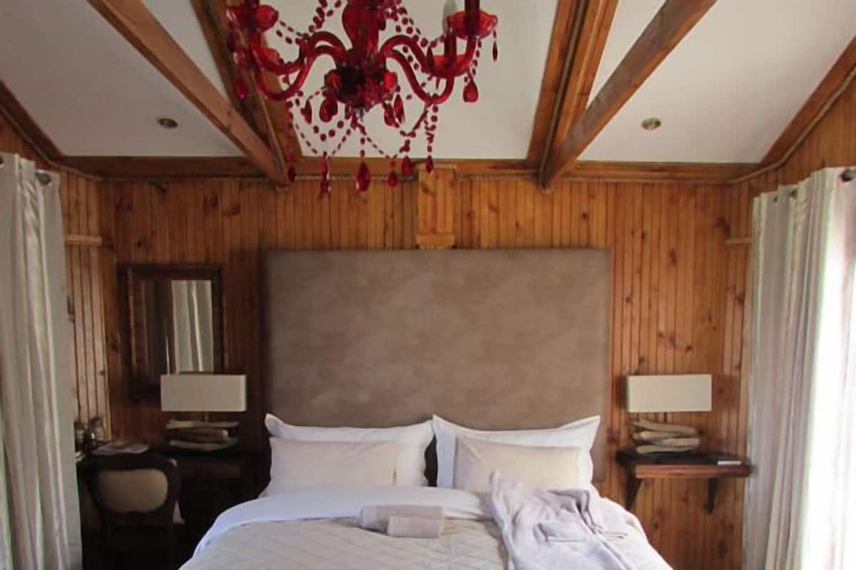 A hotel room with a large bed, wooden walls, a chandelier, two bedside tables with lamps, and a window with curtains.