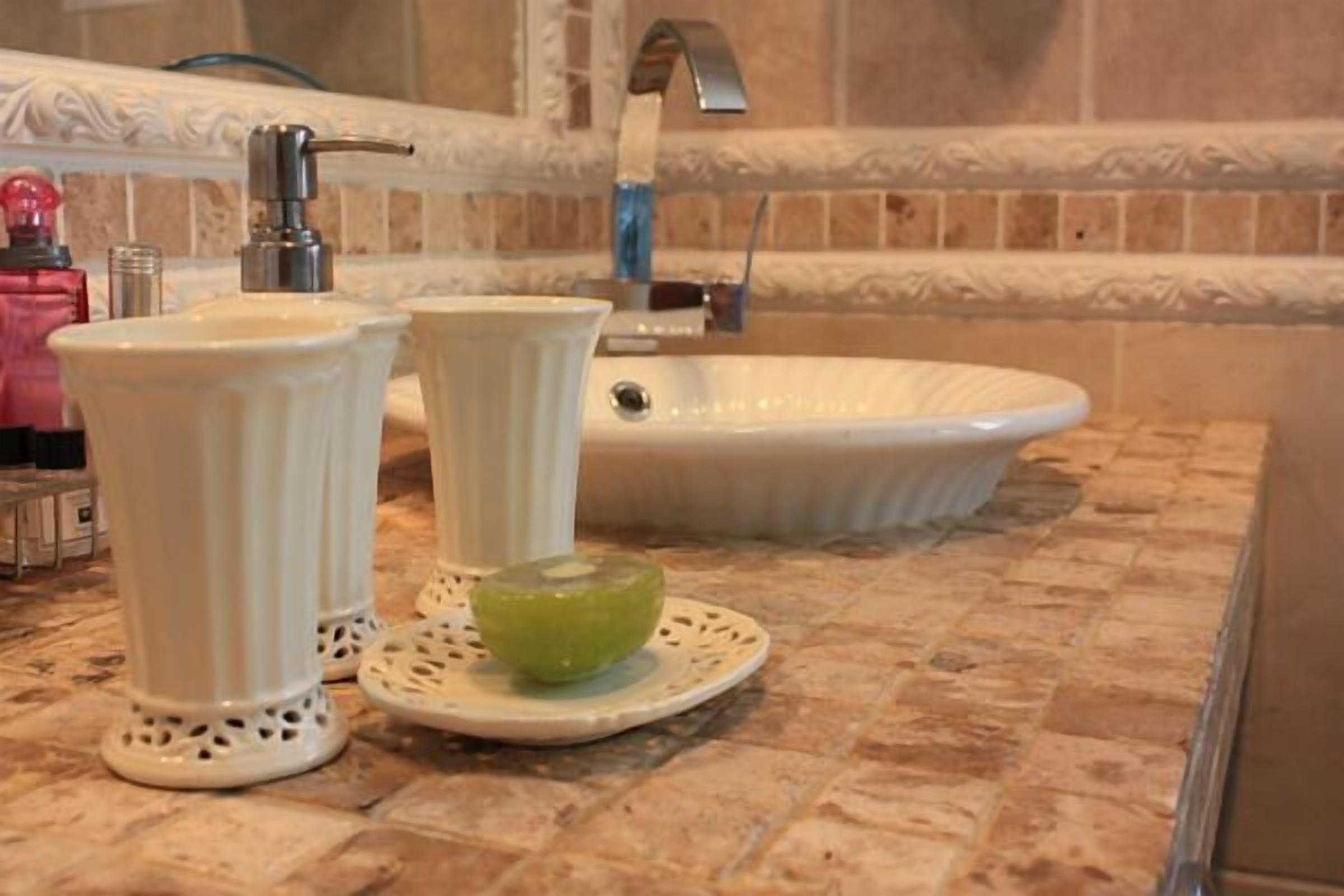 A bathroom with a white sink, two tall vases, and a green bowl on a decorative plate.