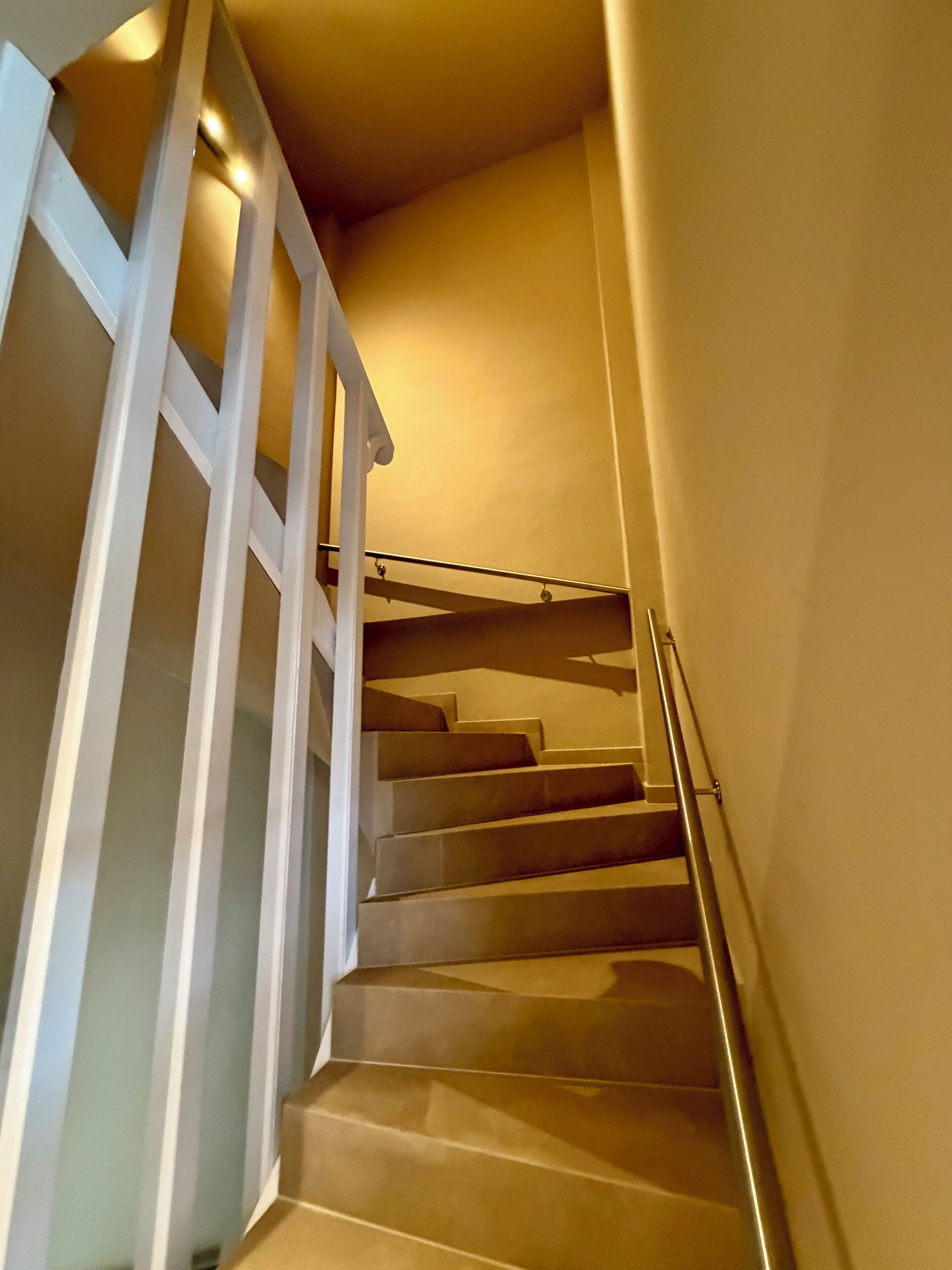 Un escalier avec des rampes et une main courante blanches, menant à l’étage supérieur.