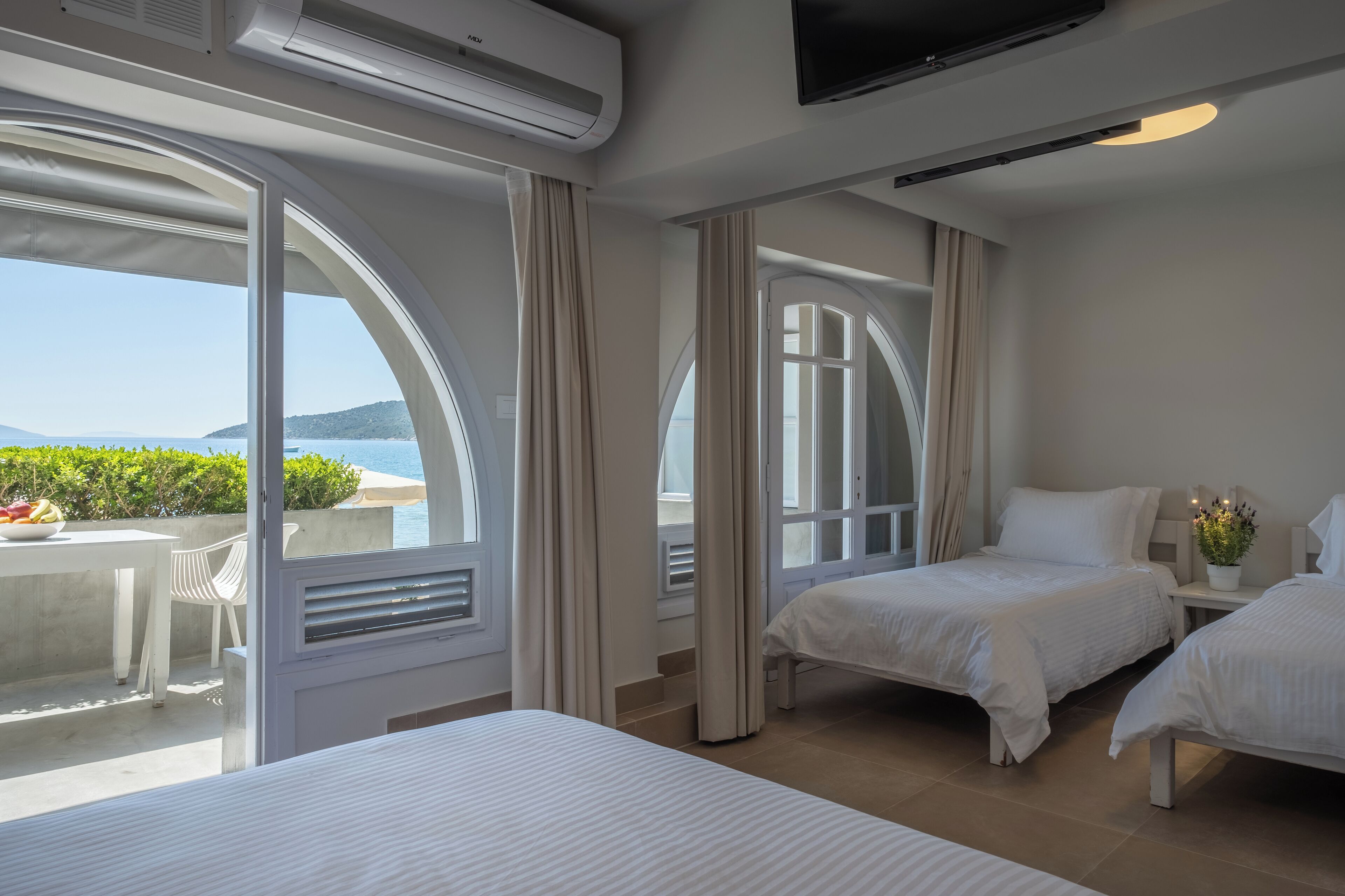 Una camera d'albergo con due letti, una televisione e un balcone vista mare.