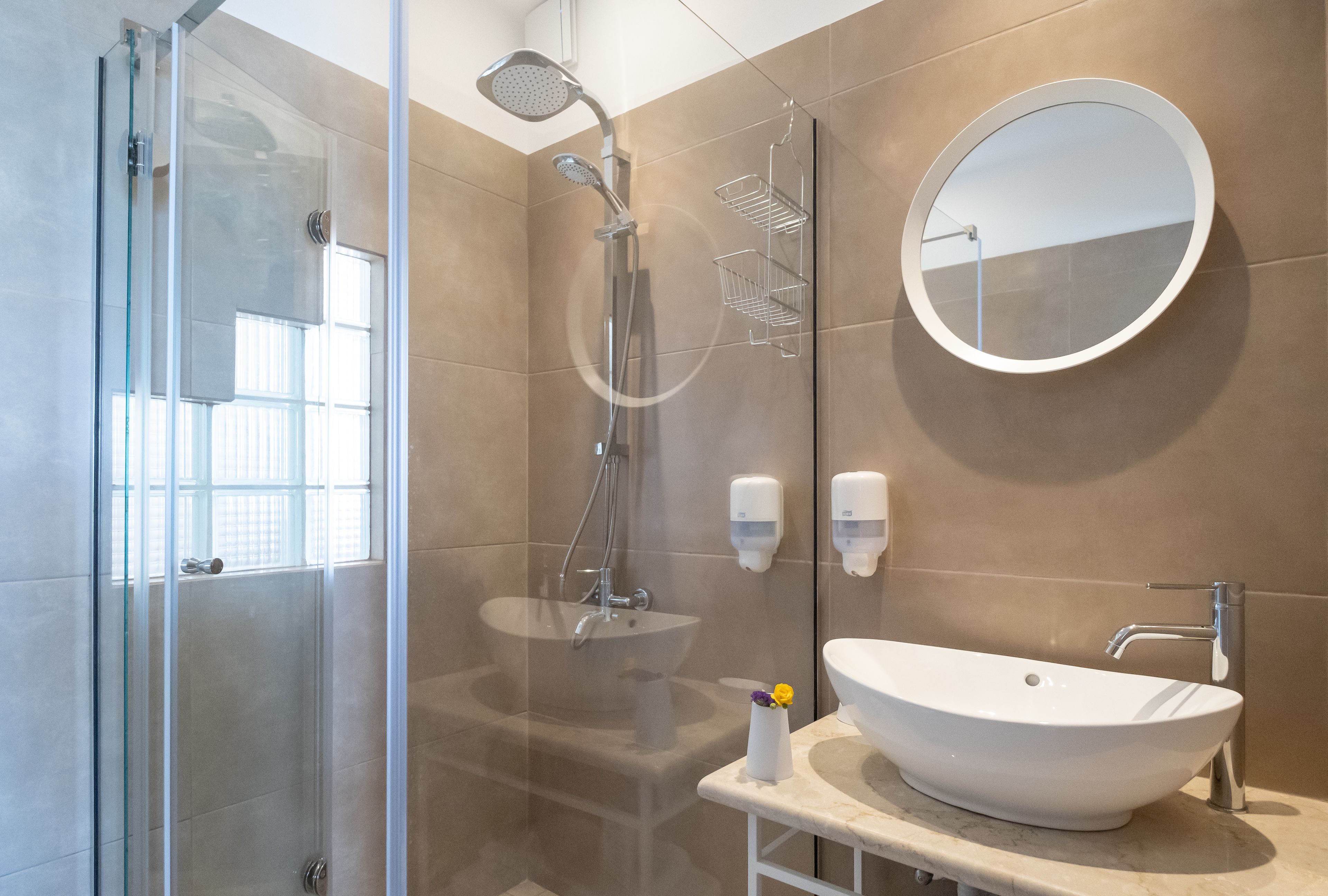 A modern bathroom with a glass shower enclosure, a white sink, and a round mirror.