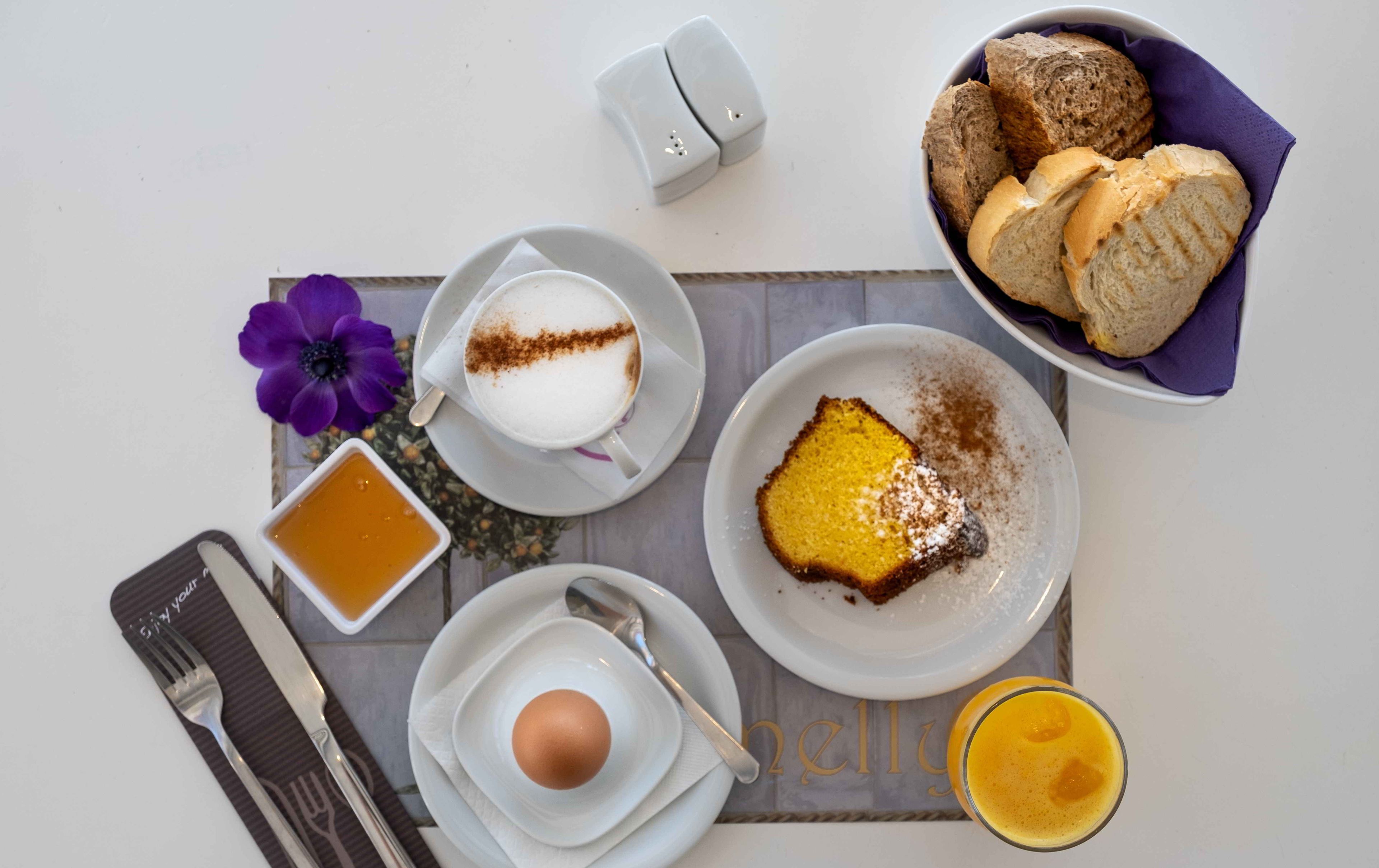 En morgenmadsopsætning med en kop kaffe, et stykke kage, en skål kiks, et glas juice og en blomst på et bord.