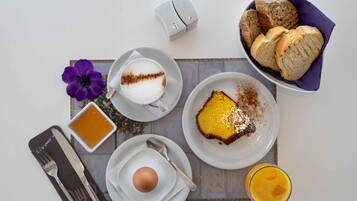 En morgenmadsopsætning med en kop kaffe, et stykke kage, en skål kiks, et glas juice og en blomst på et bord.