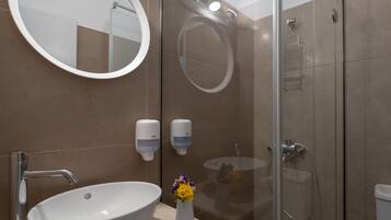 A modern bathroom with a round mirror, a sink, a glass-enclosed shower, and two soap dispensers.