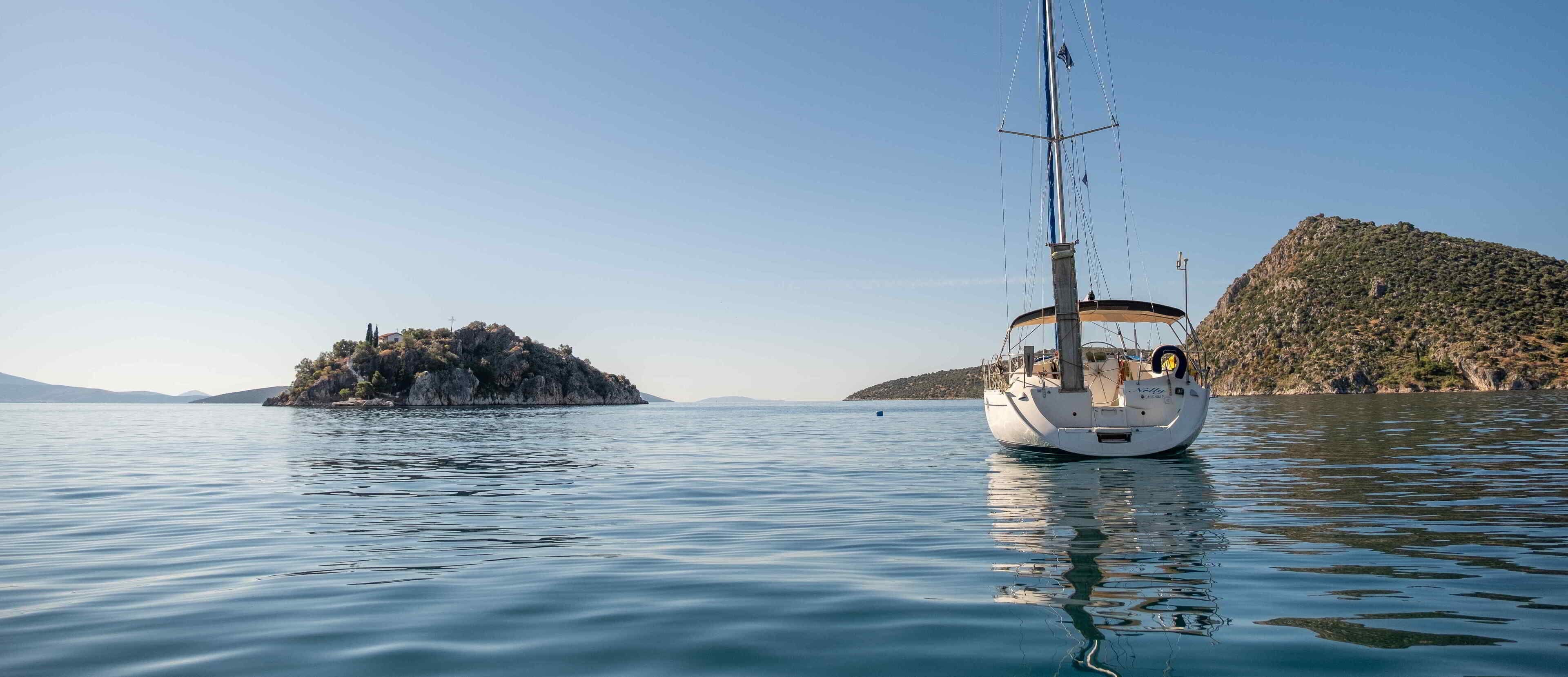 A sailboat on calm waters with a rocky island and a hill in the background.