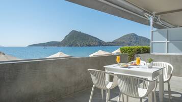 A balcony with white chairs and a table, overlooking a body of water with boats and hills in the distance.