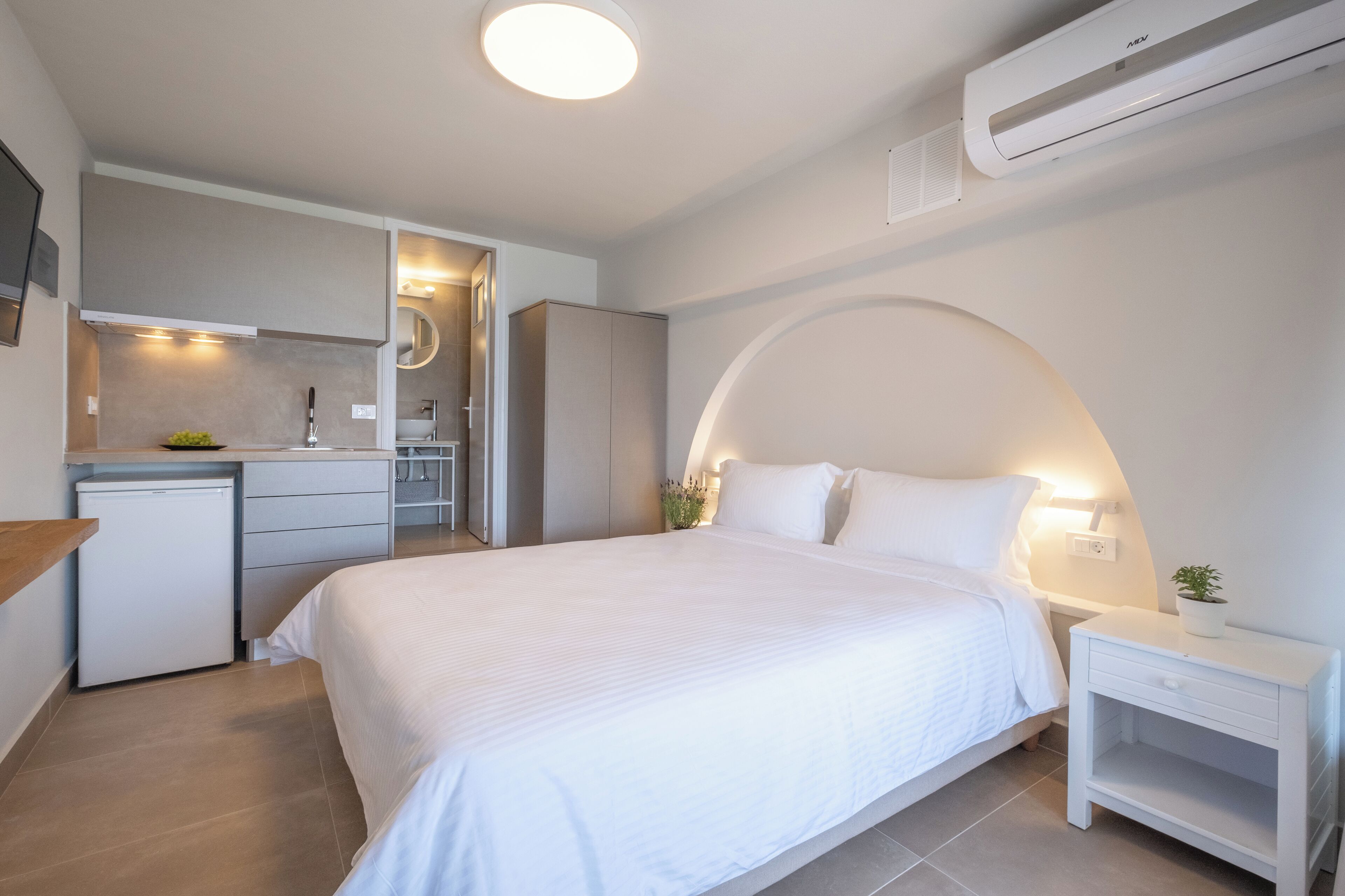 A modern hotel room with a neatly made bed, a small kitchenette, and a built-in wardrobe.