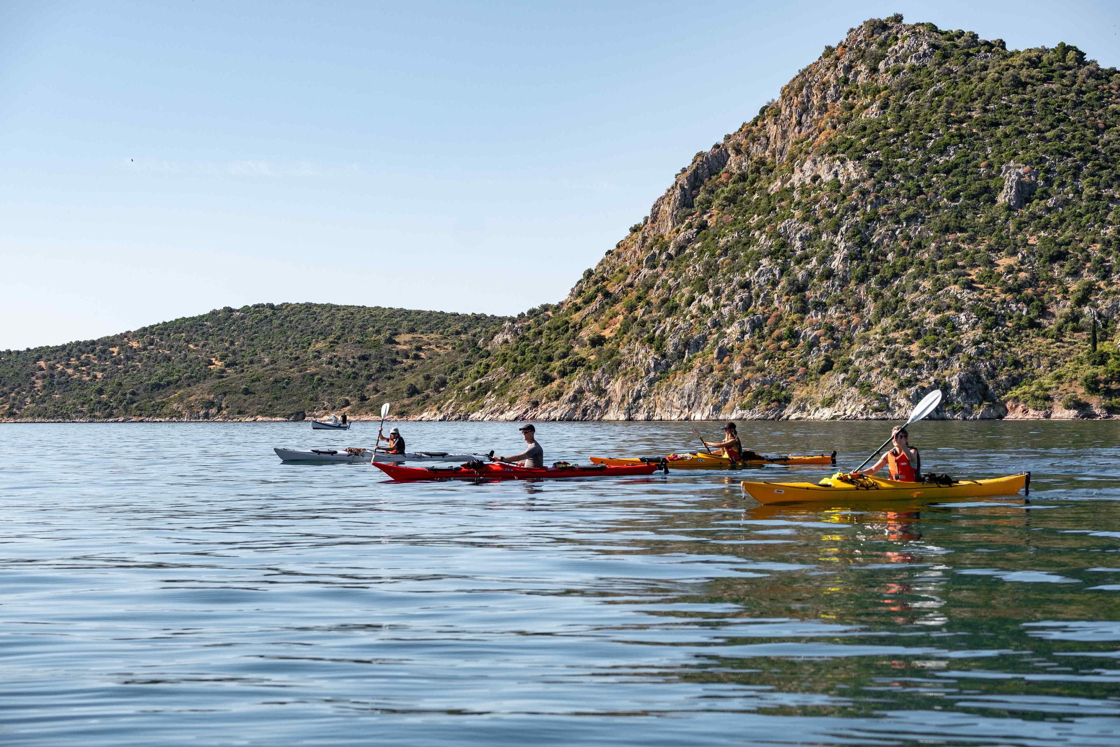 Un grupo de personas haciendo kayak en un lago tranquilo con montañas al fondo.