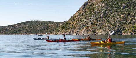 A group of people kayaking on a calm lake with a mountainous backdrop.