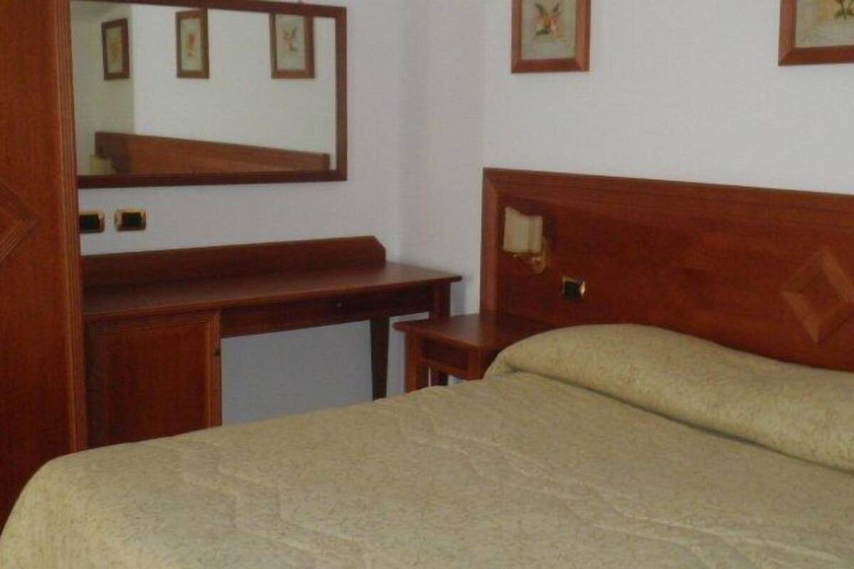 Een slaapkamer met een bed, een houten bureau, een spiegel en een nachtkastje.