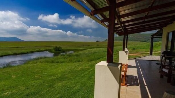 A covered outdoor area with a view of a grassy field and a small body of water.
