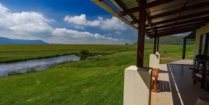 Uma área externa coberta com vista para um campo gramado e um pequeno corpo d'água.