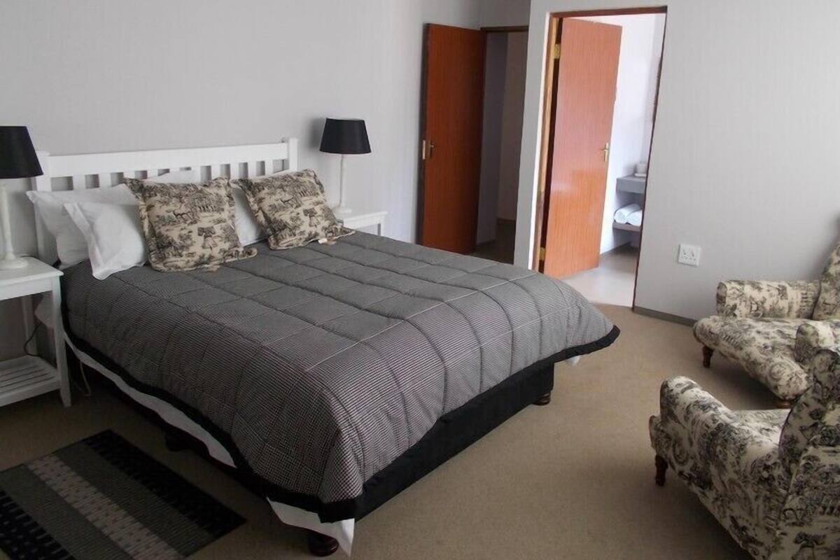 Een slaapkamer met een bed, nachtkastjes, een stoel en een deur naar een andere kamer.