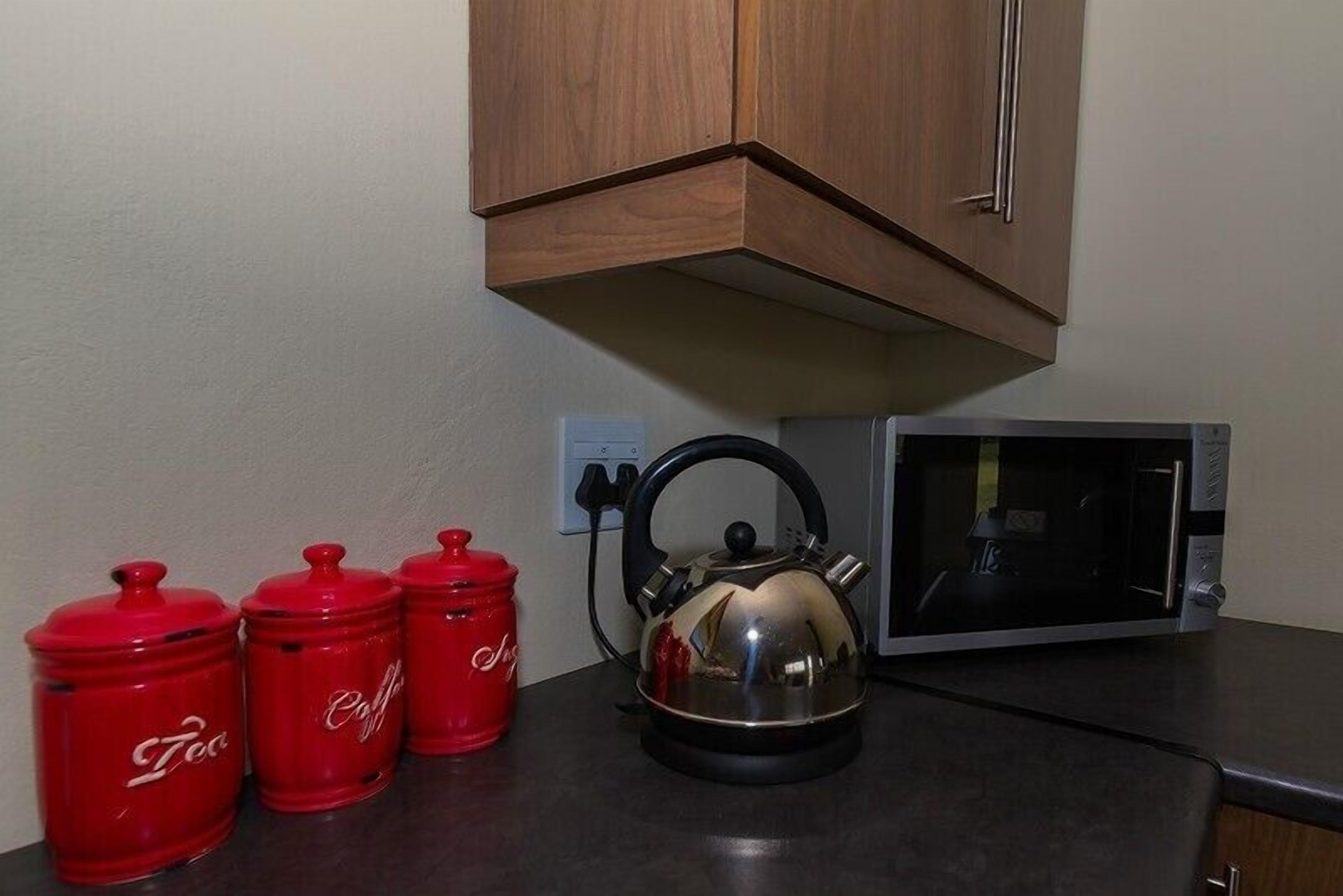 A kitchen with a kettle, a microwave, and three red containers labeled "Tea".
