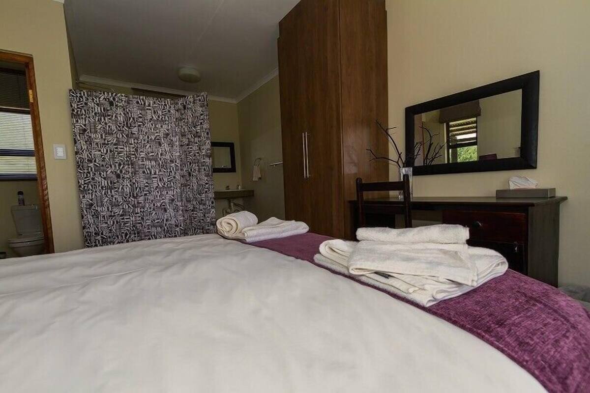Hotelkamer met een groot bed, een houten garderobe, een spiegel en een badkamer die door een open deur zichtbaar is.