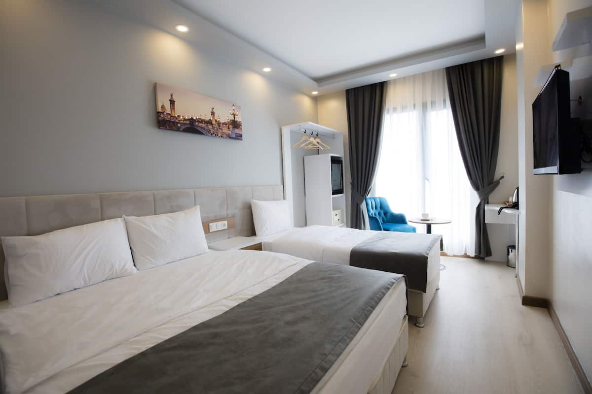 A hotel room with two beds, a television, a desk, and a window with curtains.