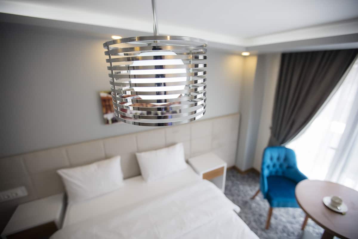 A modern hotel room with a large bed, a blue armchair, a small table, and a unique hanging light fixture.