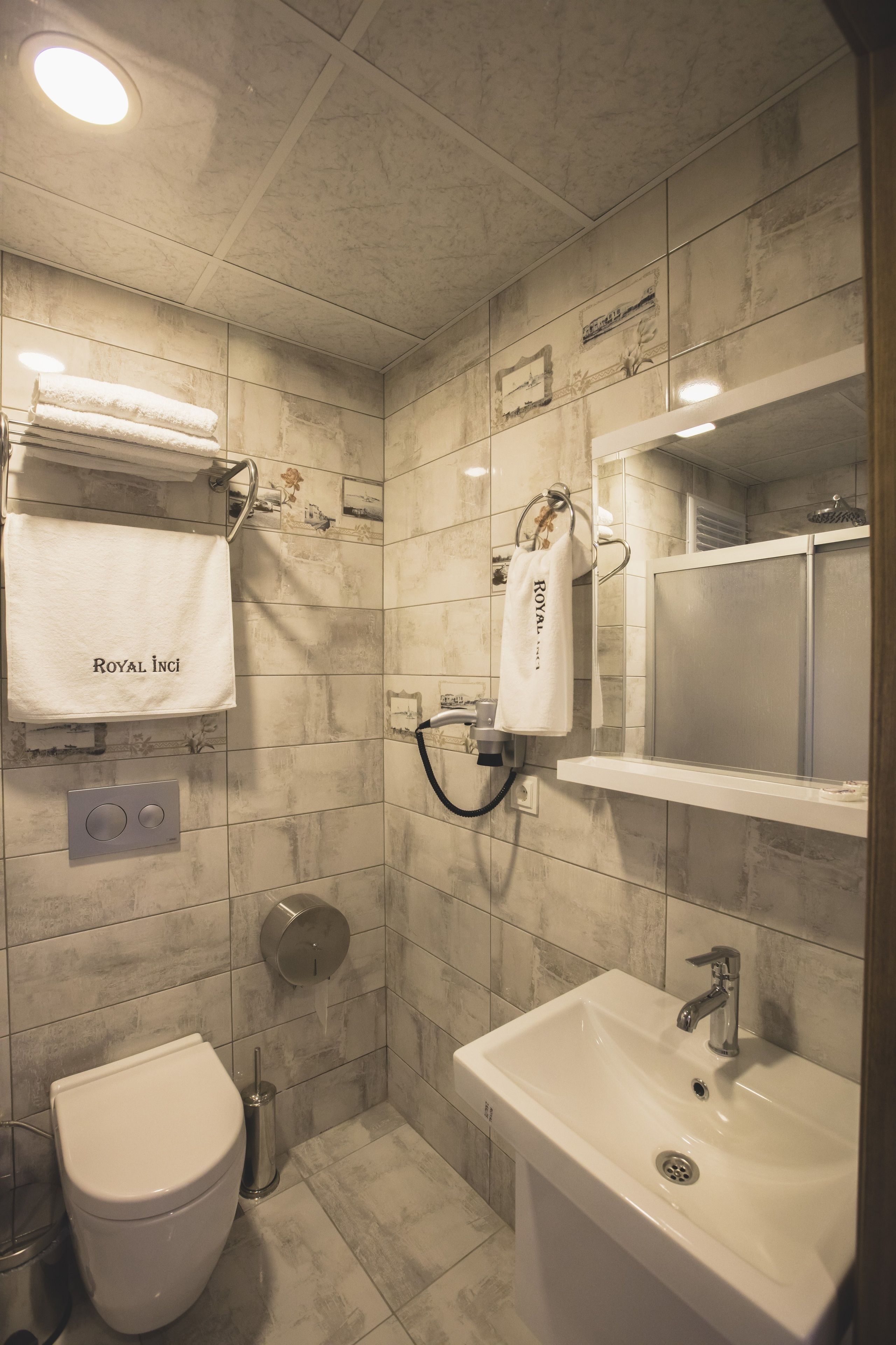 A bathroom with a toilet, sink, and shower. There are towels hanging on hooks and a mirror above the sink.