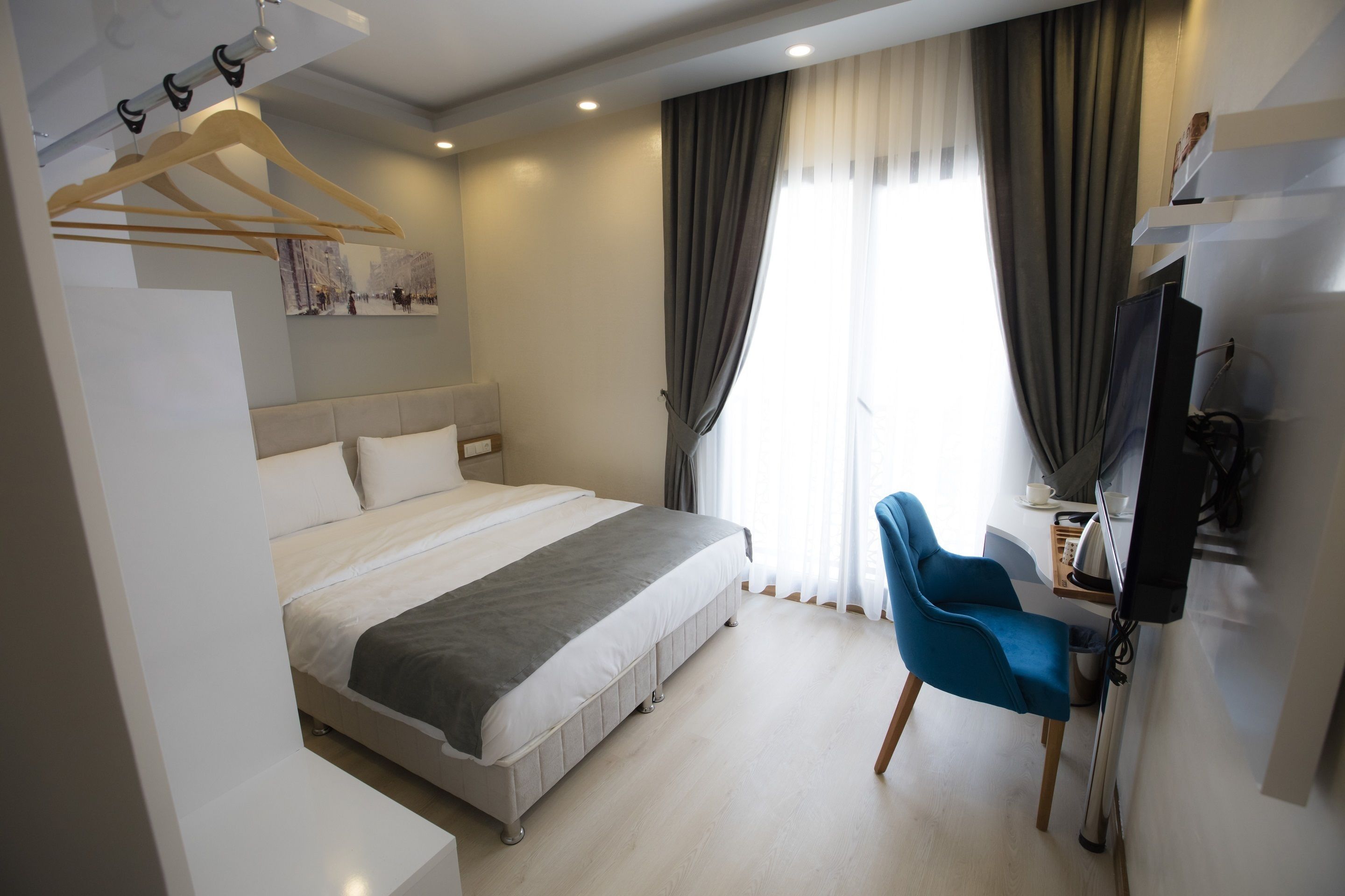 A modern hotel room with a large bed, a desk with a chair, a television, and a window with curtains.
