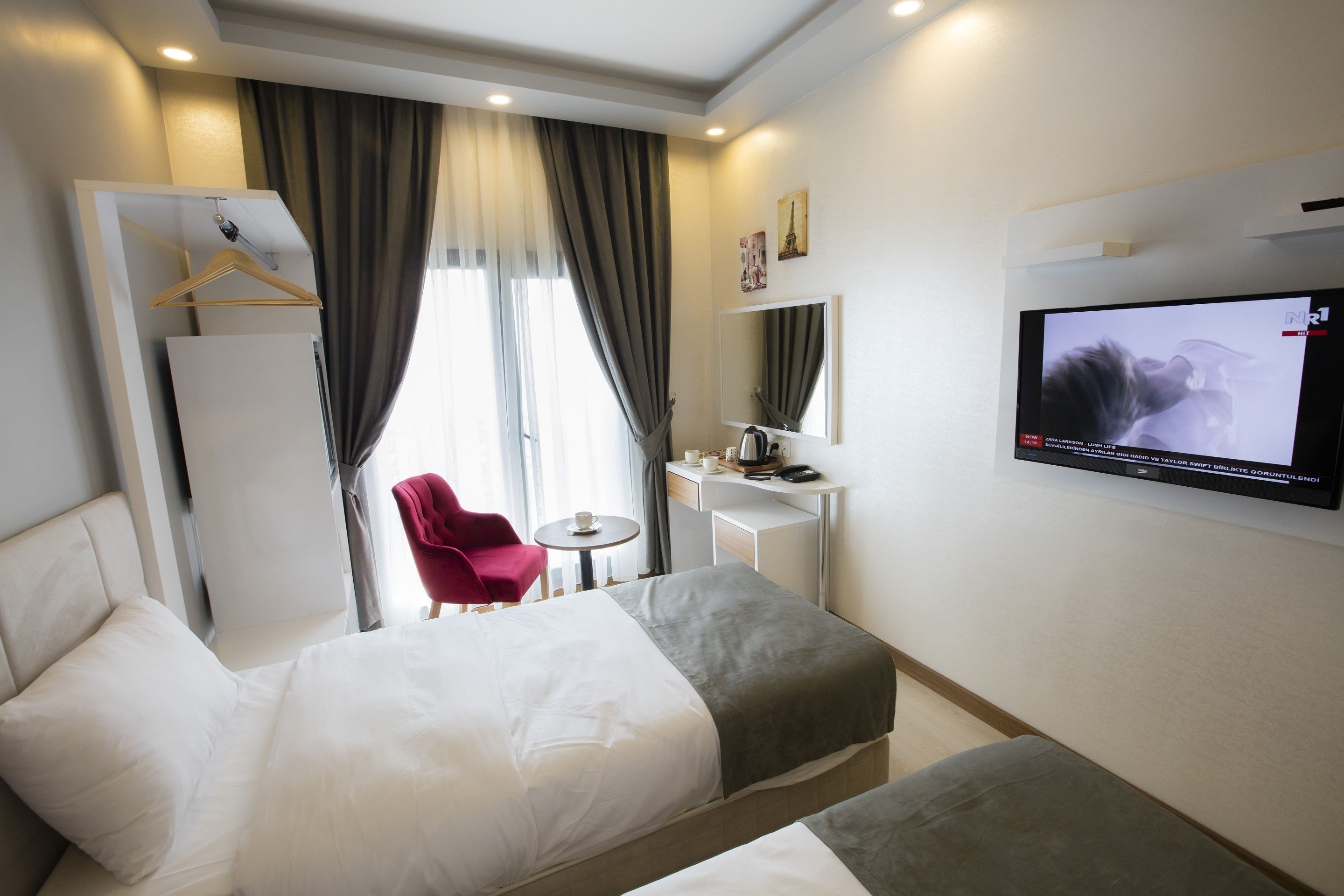 A hotel room with two beds, a desk, a chair, a TV, and a window with curtains.