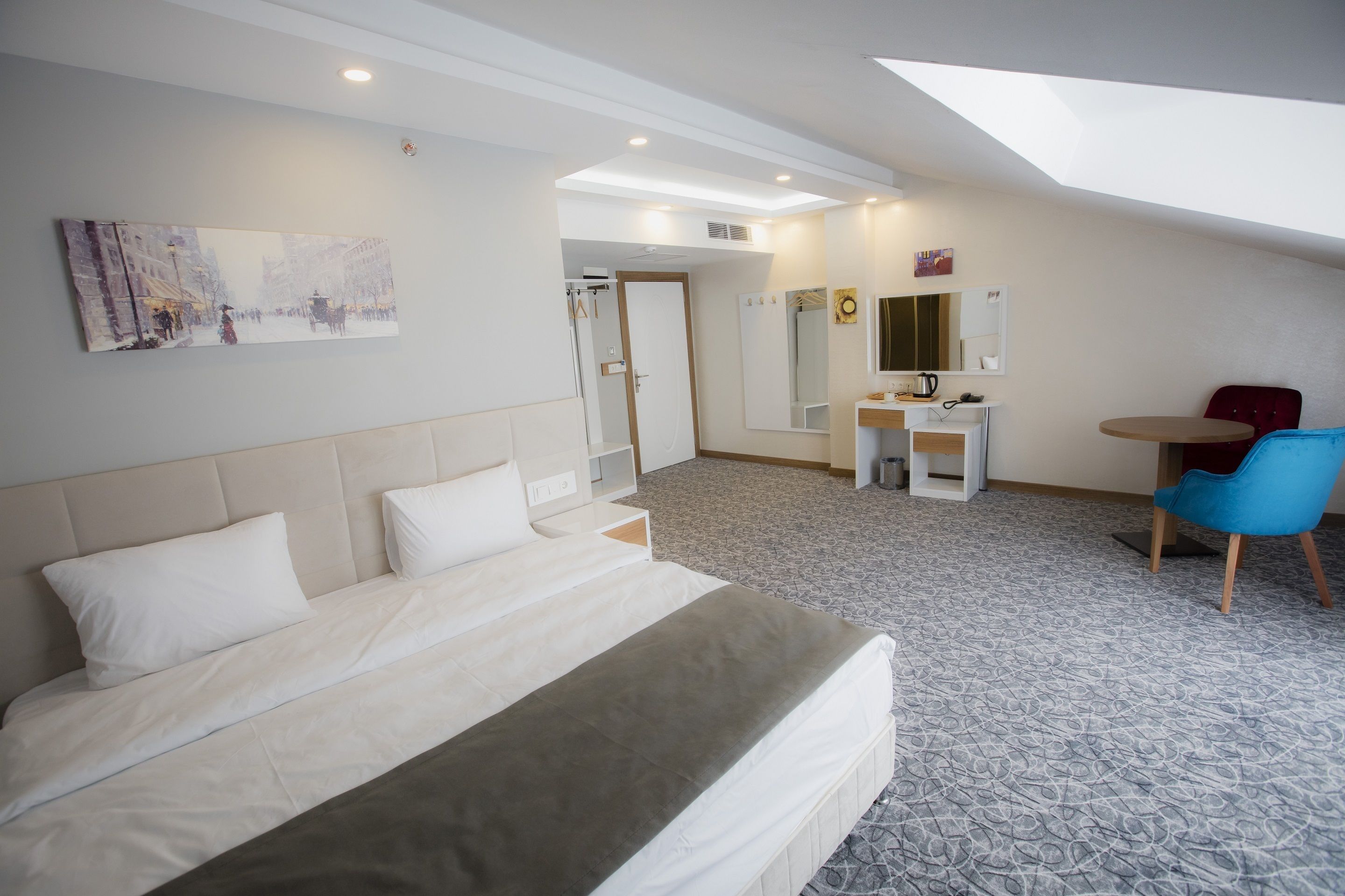 Ett hotellrum med en stor säng, ett skrivbord, en stol, en spegel och en tavla på väggen.